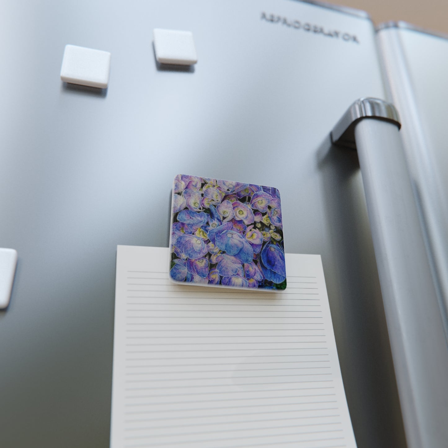 Floral magnet on a refrigerator next to a notepad