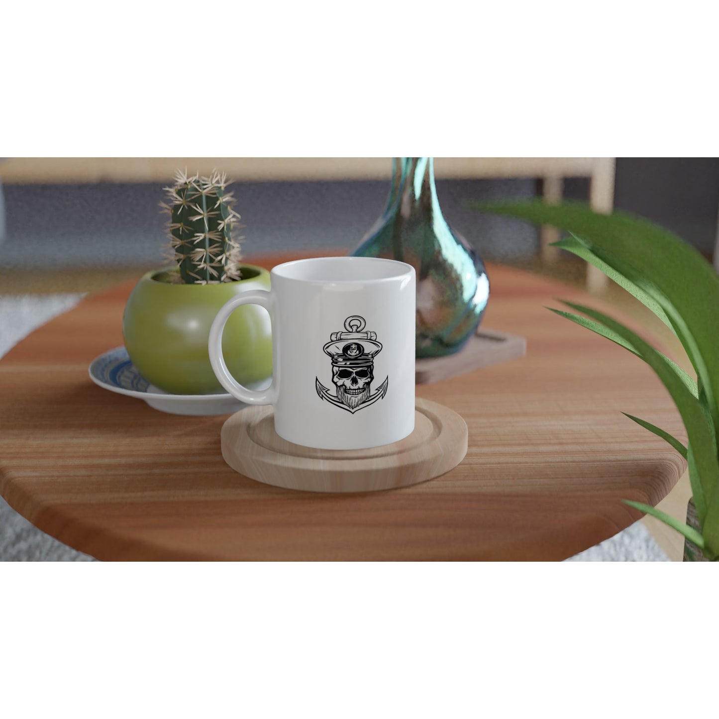 White mug with a Black and white illustration of a skull with a captain's hat, a beard, with an anchor behind it on a wooden table with a potted cactus and a green vase.