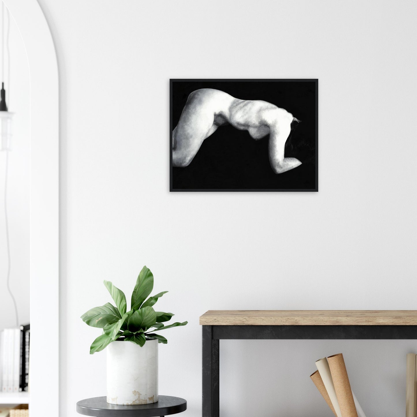 Framed black and white artwork of a reclining nude female figure on a wall above a desk with a plant.
