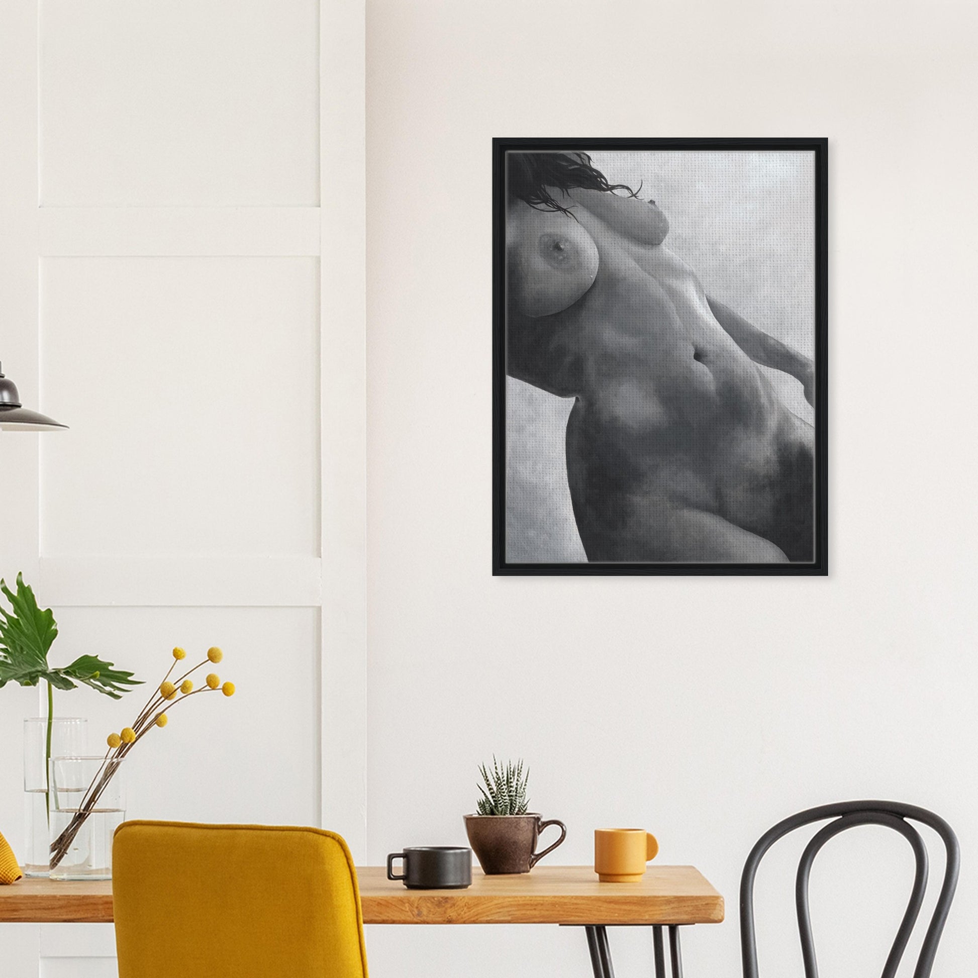 Framed black and white artwork of a nude figure on a wall above a dining table with chairs.