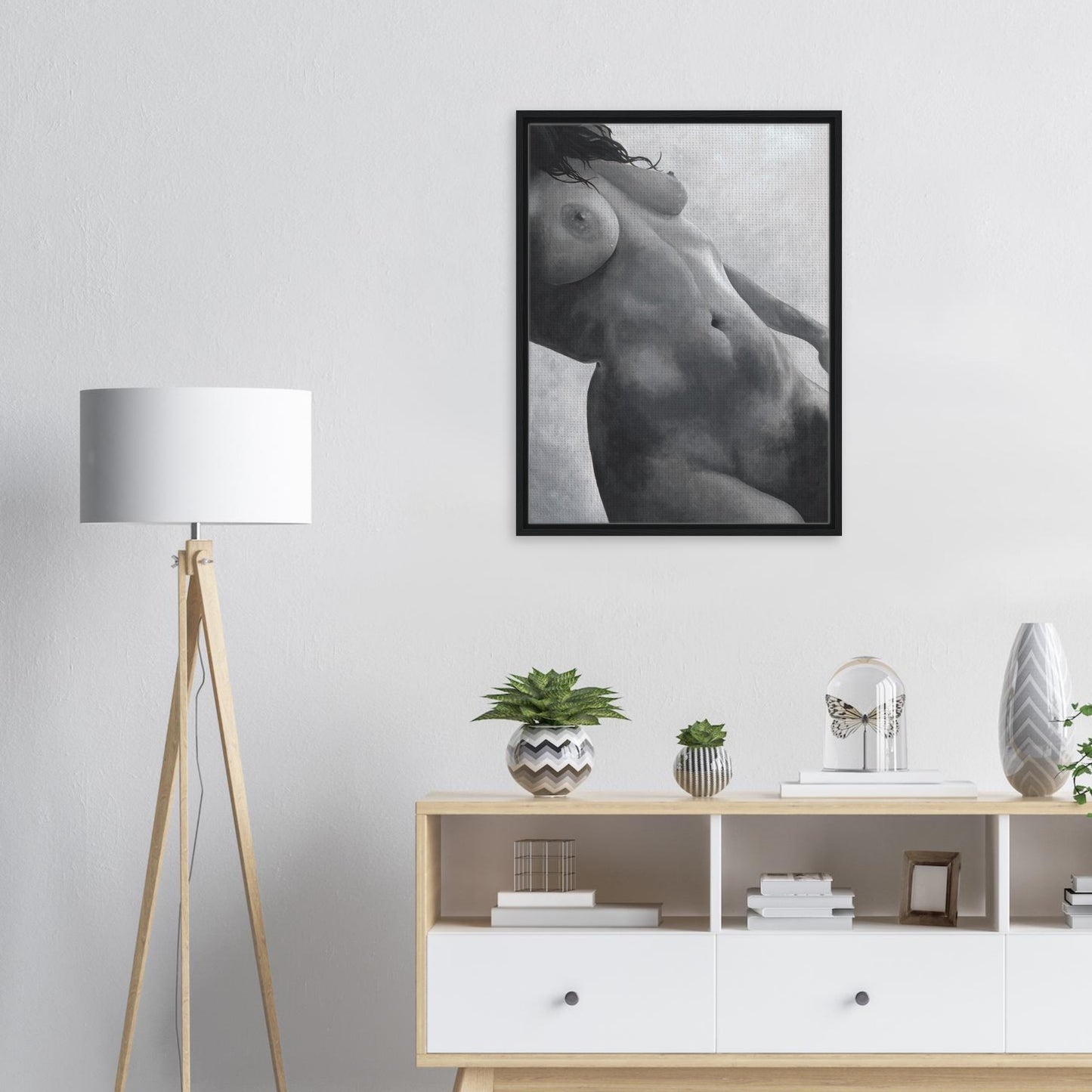 Framed black and white artwork of a nude figure on a wall above a wooden sideboard with decorative items.