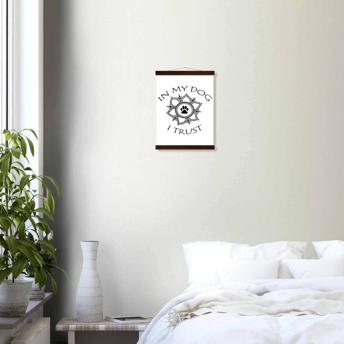Poster with 'In my dog I trust' text around a  paw print mandala design with a Light colored hanging poster frame with a top and a bottom only  a  white wall above a bed and home decor on a wide table