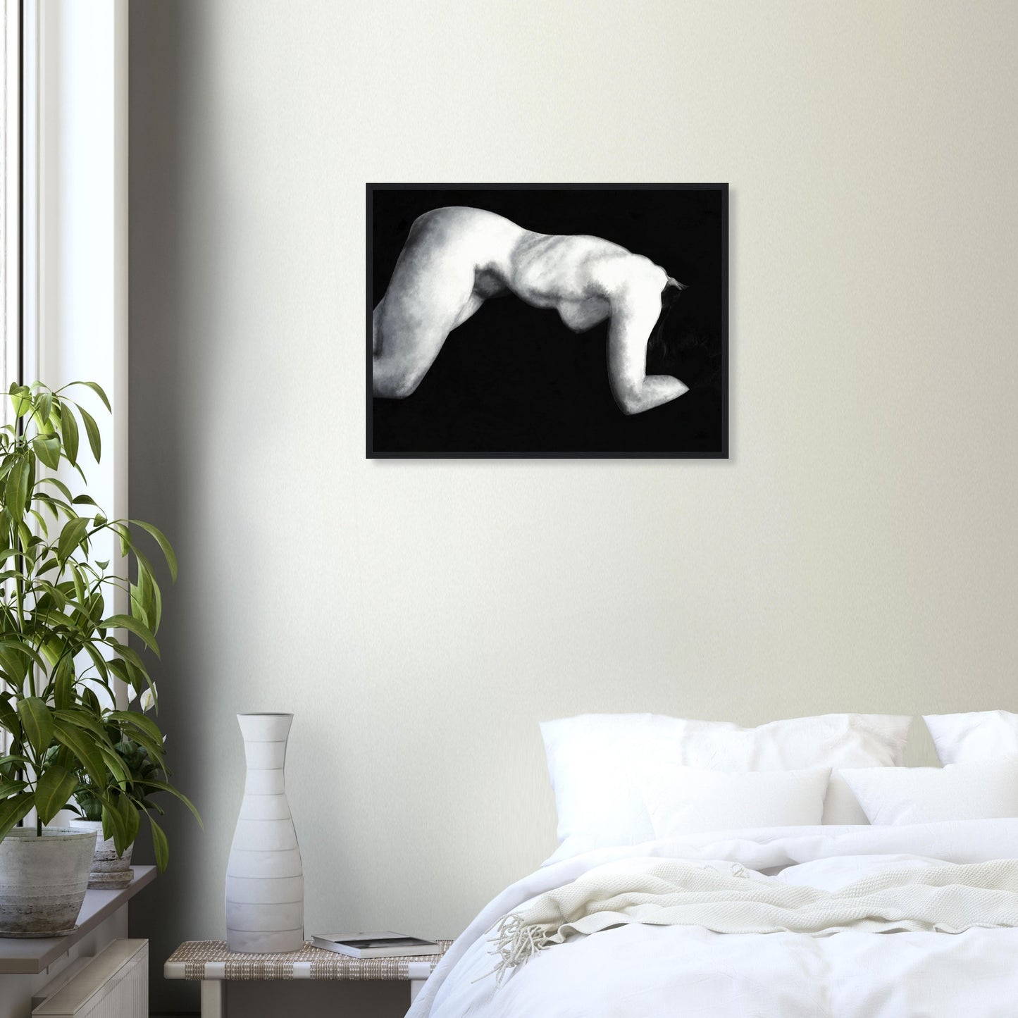 Framed with a black frame, a black and white artwork of a reclining nude female figure on a wall above a bed in a bedroom.