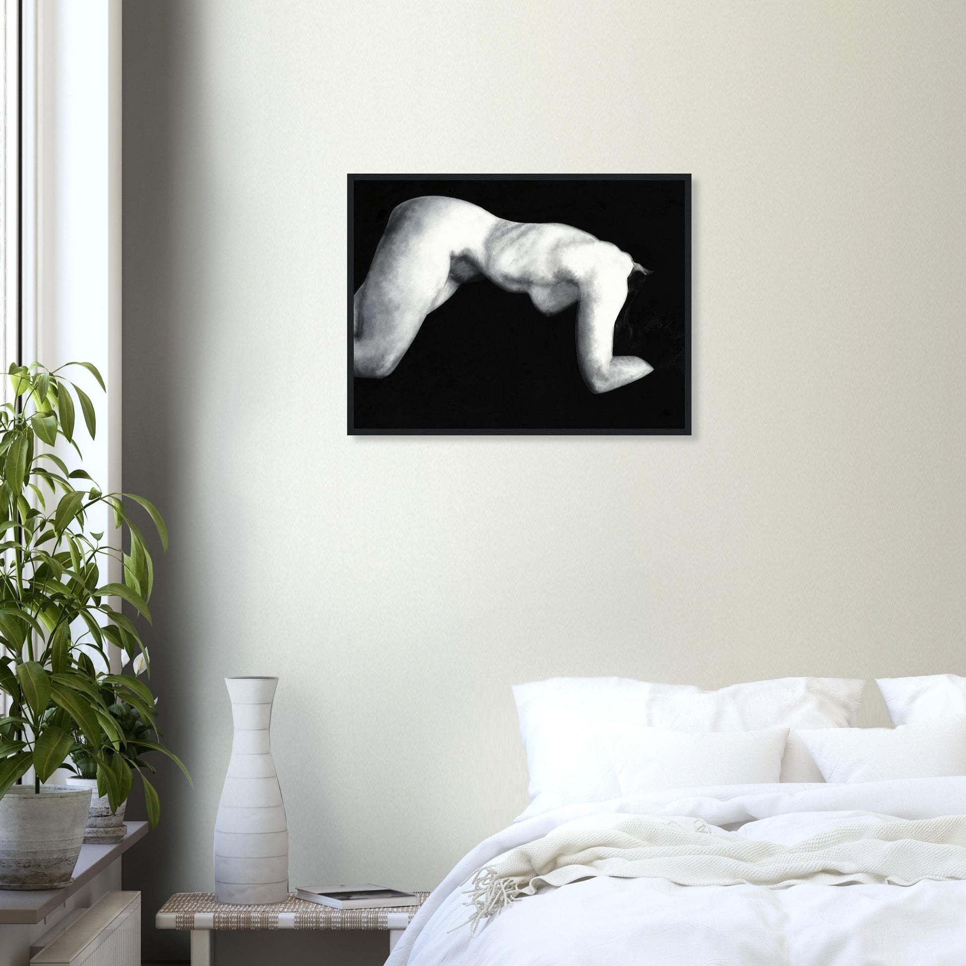 Framed with a black frame, a black and white artwork of a reclining nude female figure on a wall above a bed in a bedroom.