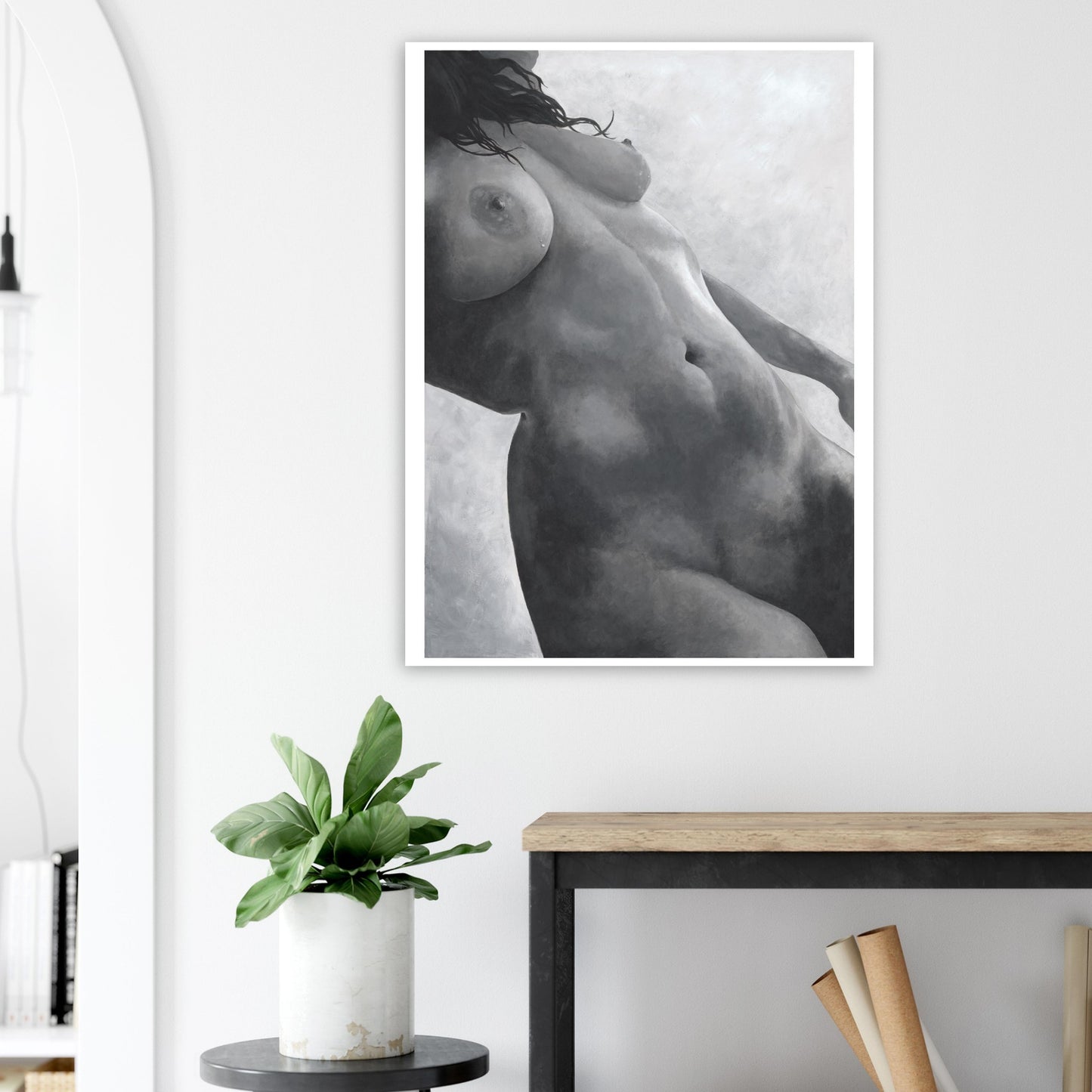Framed black and white artwork of a nude figure on a wall above a desk with a plant.