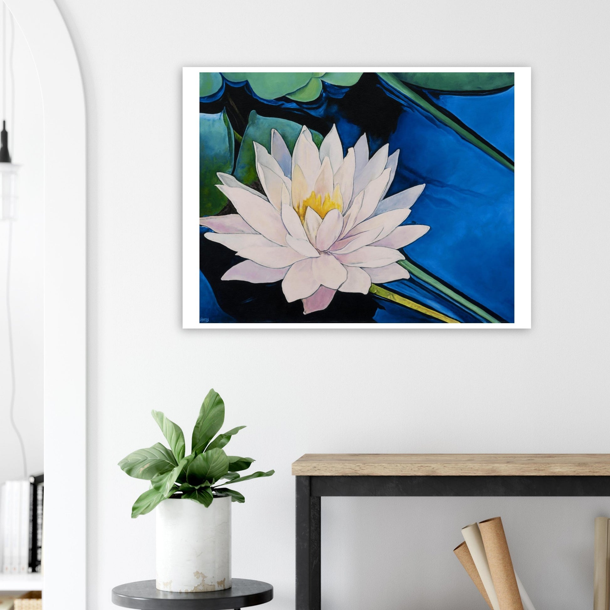 Framed artwork of a water lily on a wall above a desk with a plant.