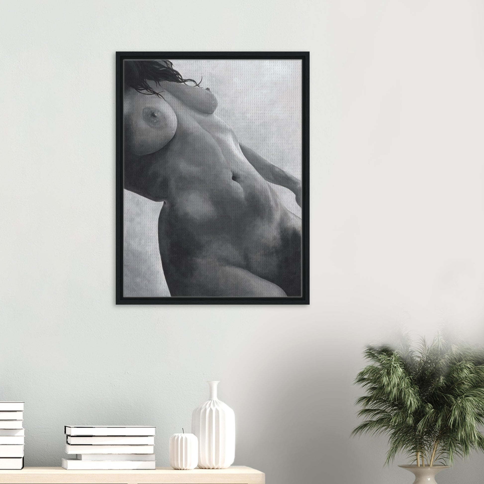Framed black and white artwork of a nude figure on a wall with decor items below.