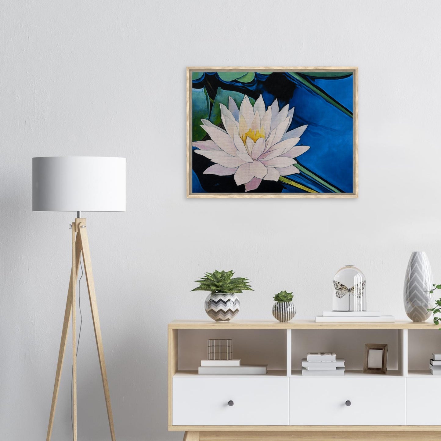Framed artwork of a water lily on a wall above a wooden cabinet with decorative items.